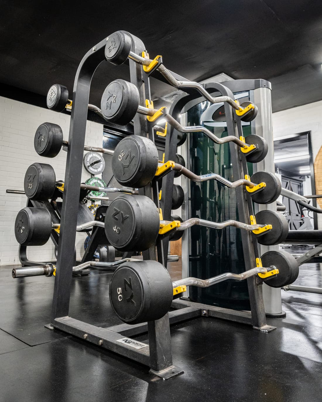 A vertical rack of pre-loaded barbells and EZ curl bars in front of the gym mirrors