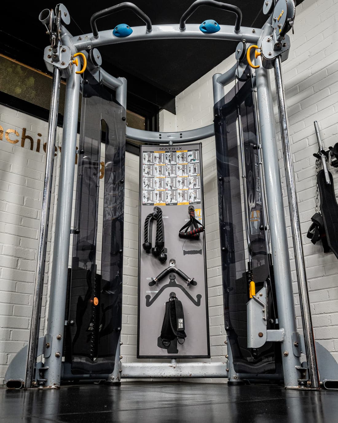 A dual-cable functional trainer with a pull-up bar, and its handles, ropes and bars stored on the wall board behind it