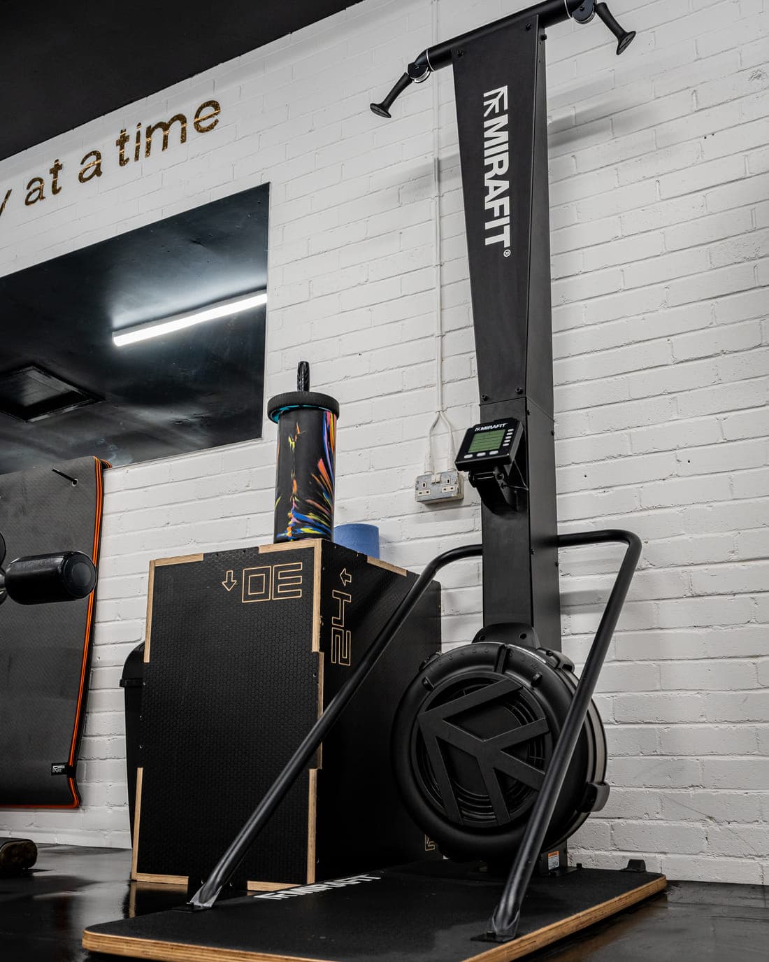 A wall-mounted ski erg with its pull handles and monitor, next to a wooden plyometric box on a lifting platform
