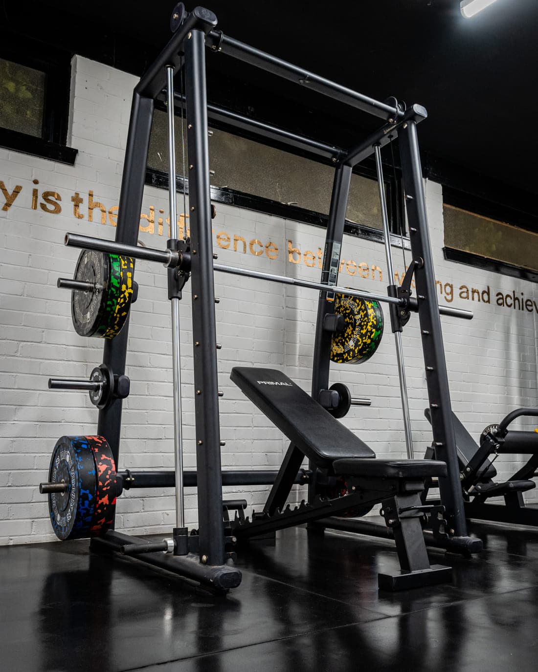 A Smith machine with a loaded bar and an adjustable bench, with colour-flecked bumper plates stored on the uprights