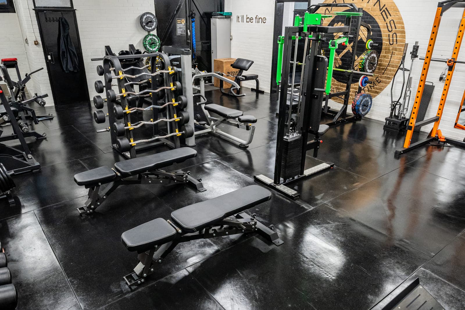 The strength area at ODAAT Fitness — a barbell rack, adjustable benches and a cable stack, with the gold ODAAT roundel on the far wall