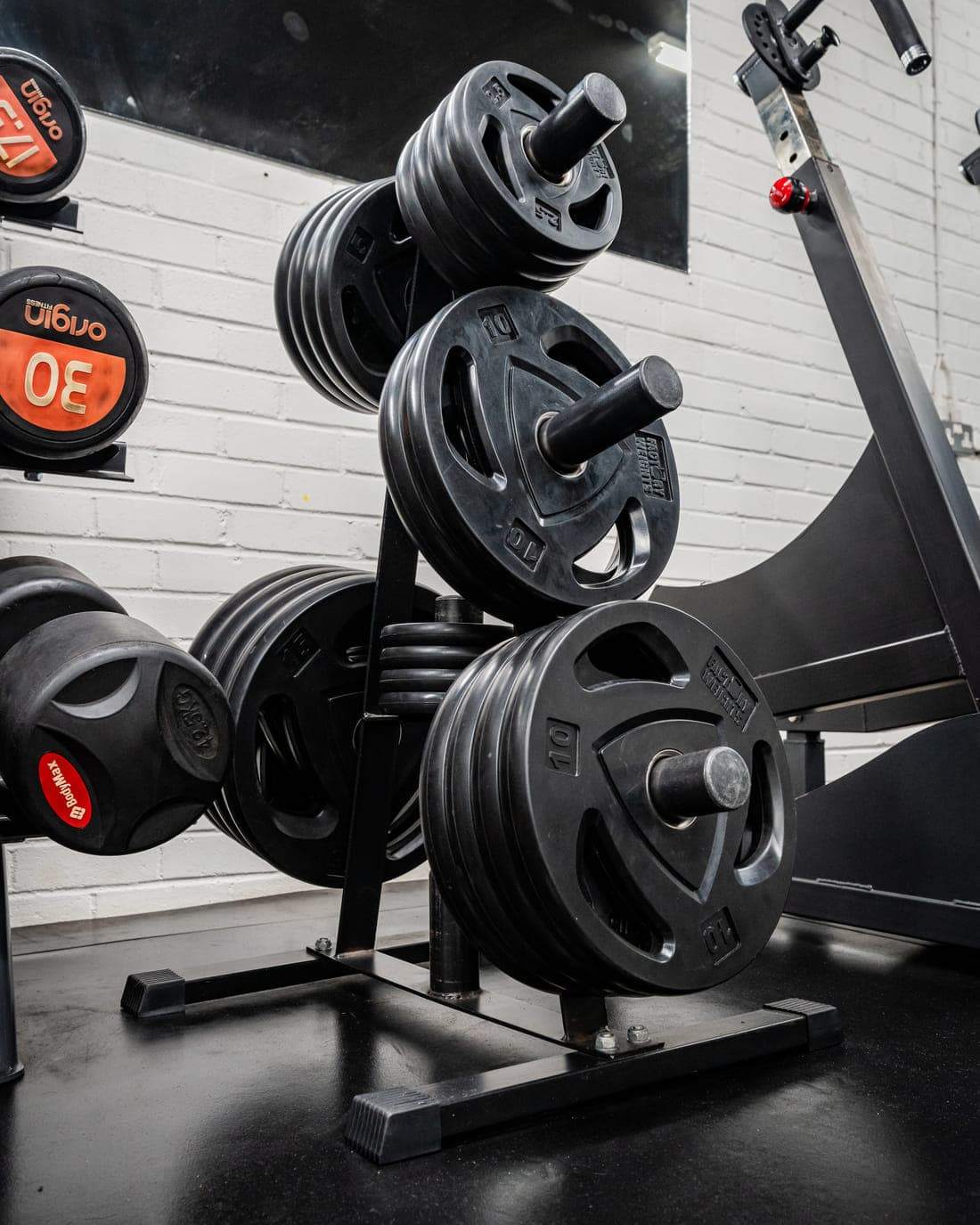 A weight tree stacked with cast-iron Olympic plates beside a rack of loaded barbells